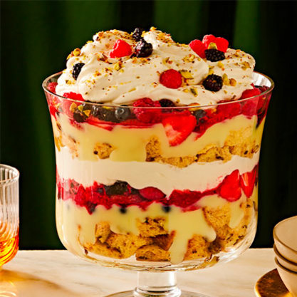 Layered holiday trifle in a glass bowl with panettone, custard, whipped cream, and mixed berries, topped with chopped pistachios.